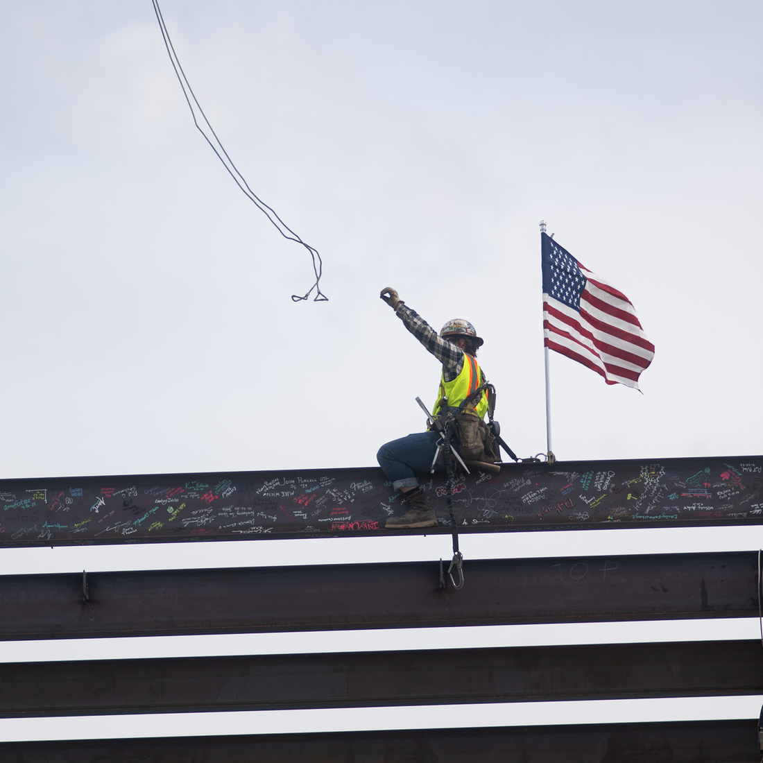 A construction worker throws off a wire attached to a crane that just lowered a beam onto a building's frame.
