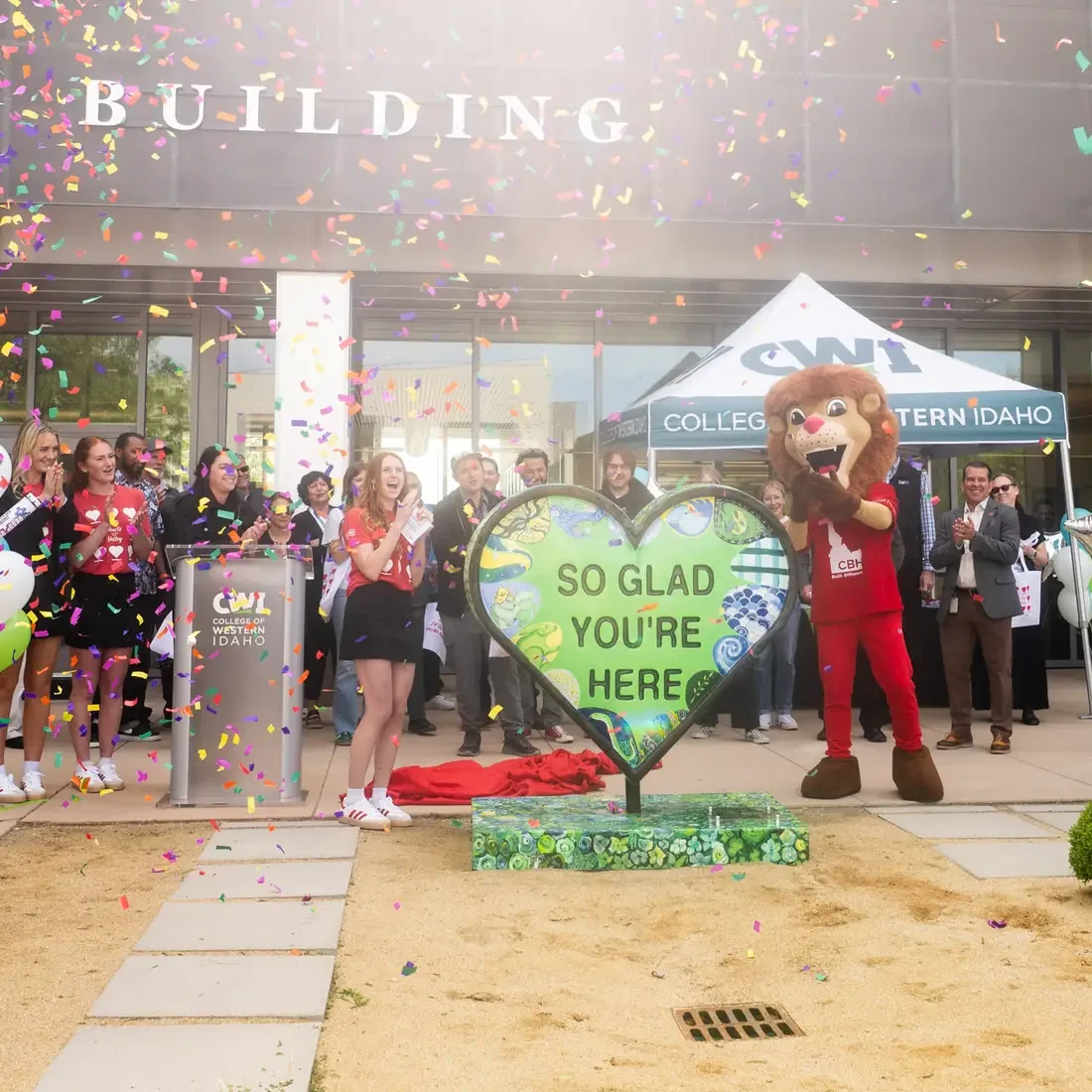 Students and a lion mascot applaud as a new sculpture is unveiled.