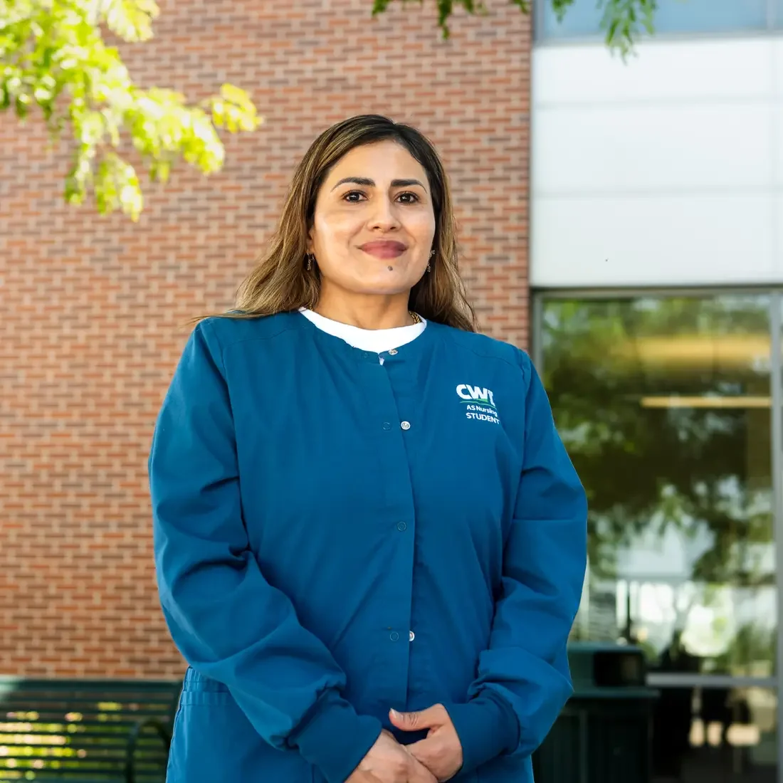 A student wearing nursing scrubs poses for a portrait in front of a brick building.