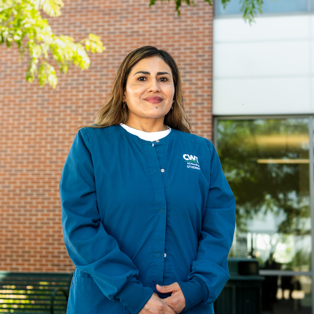A student wearing nursing scrubs poses for a portrait in front of a brick building.