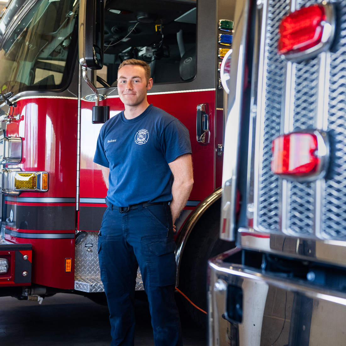 A firefighter poses for a photo in front of a firetruck.