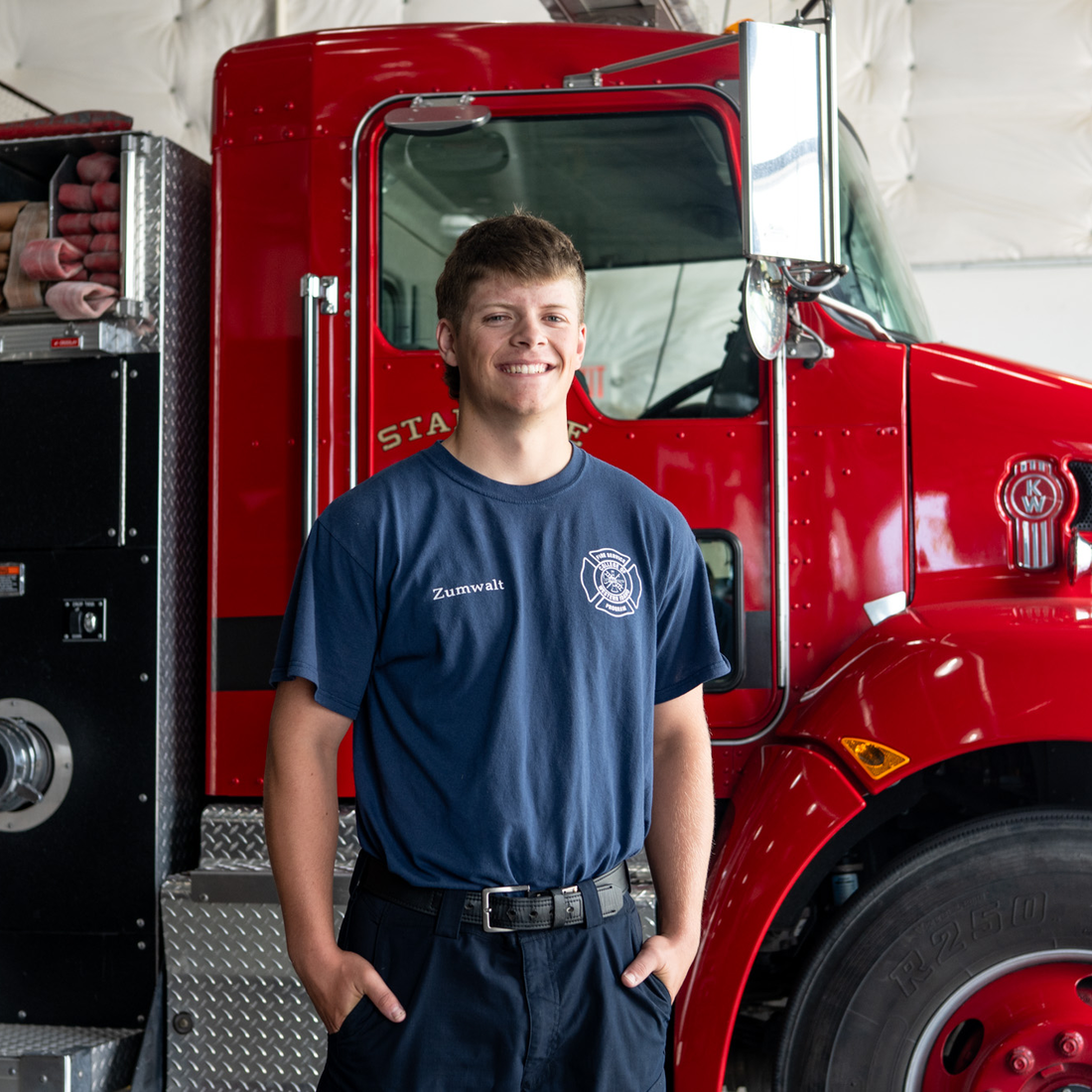 A firefighter poses for a photo in front of a firetruck.