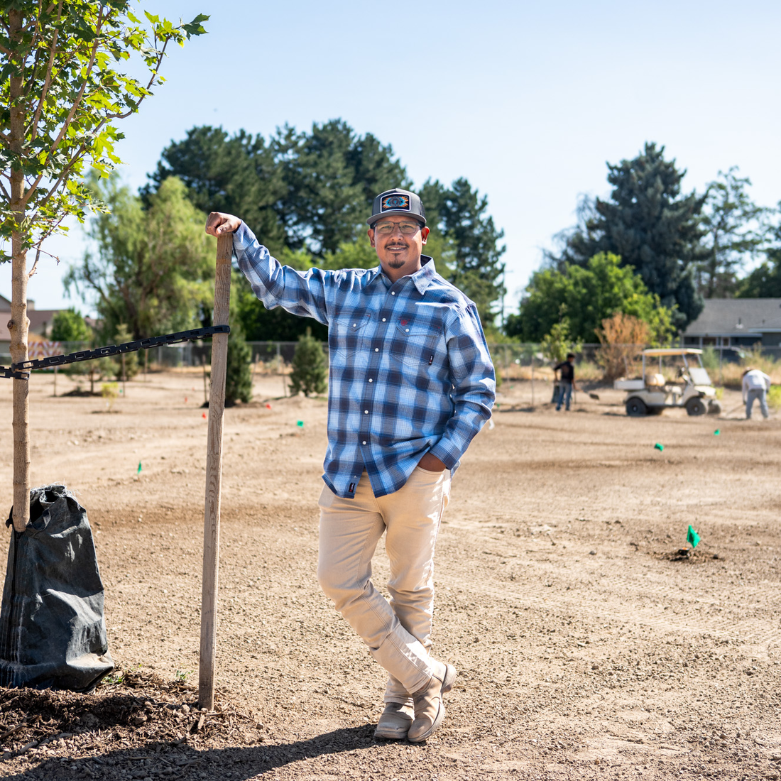 A man stands in a field with newly planted trees and employees working behind him.