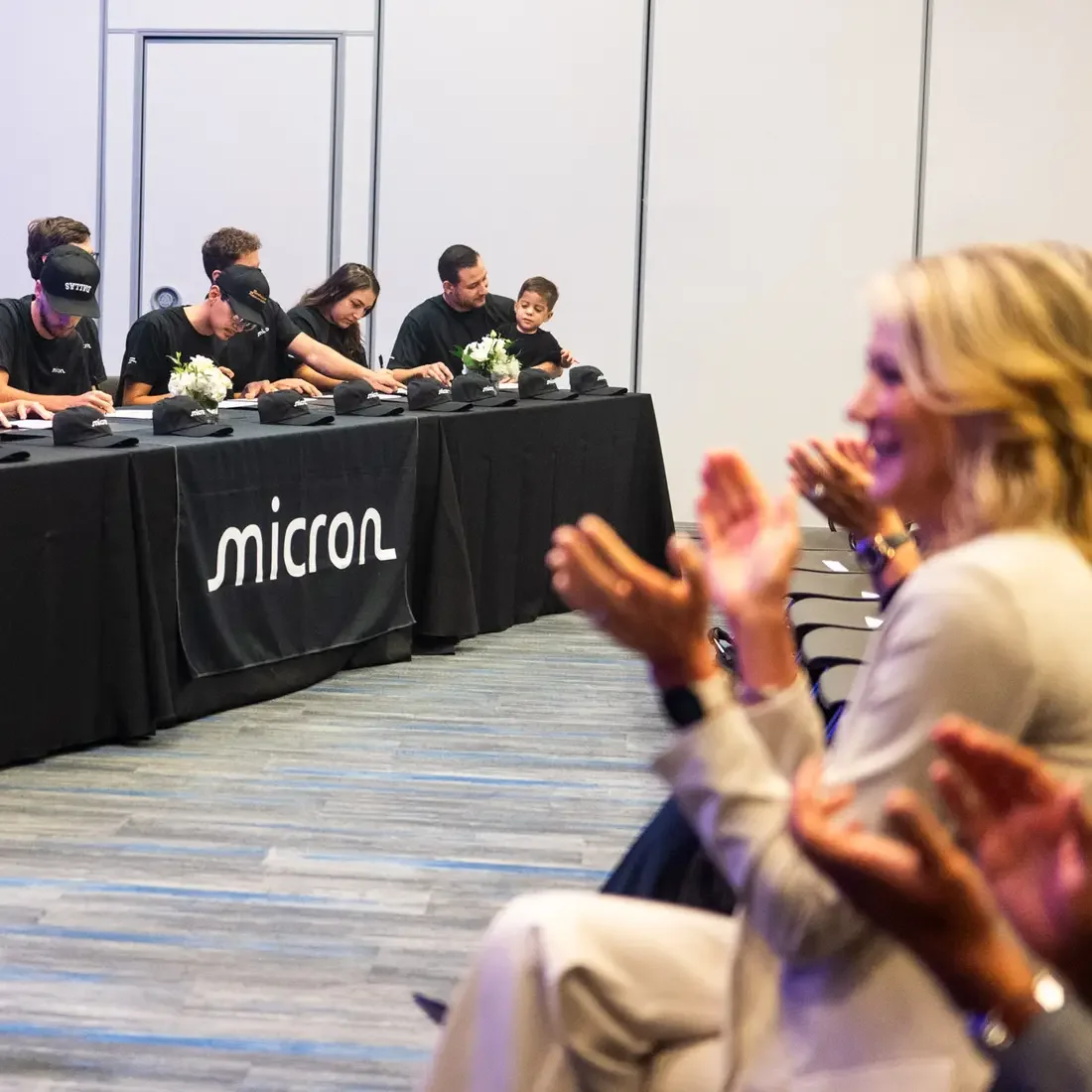 New apprentices sign certificates while an audience applaudes.