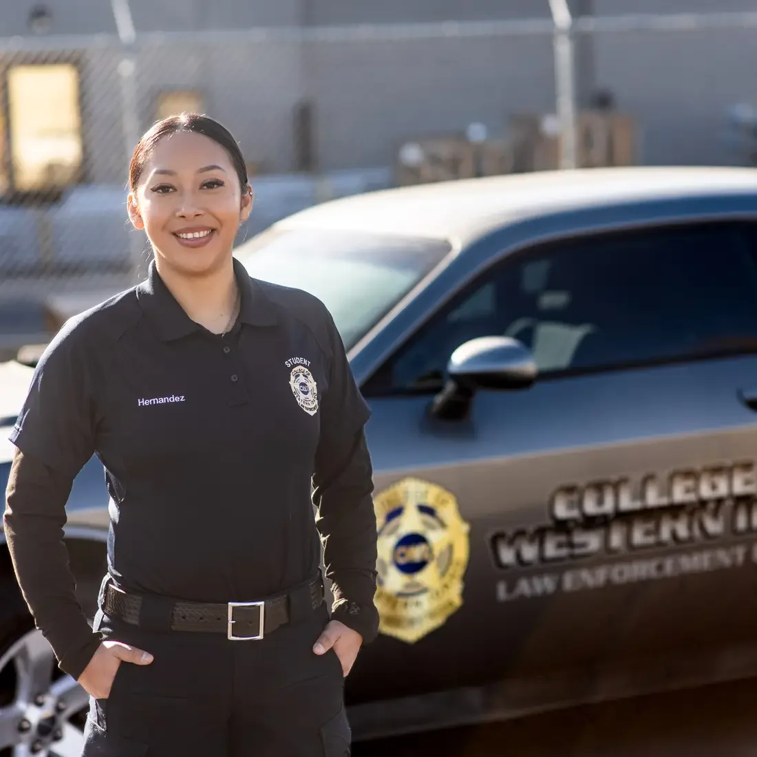 A law enforcement student stands for a portrait in front of a patrol car.