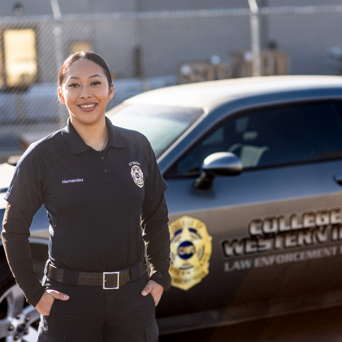 A law enforcement student stands for a portrait in front of a patrol car.