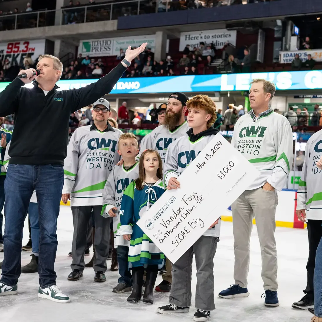 People stand on the ice as a man with a microphone address the audience at a hockey game.
