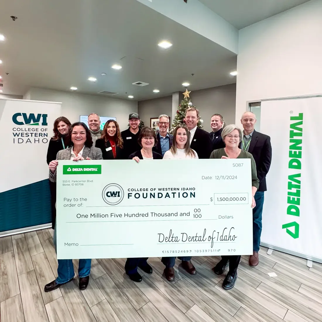 A group of people stand behind a giant check of a donation to a college.