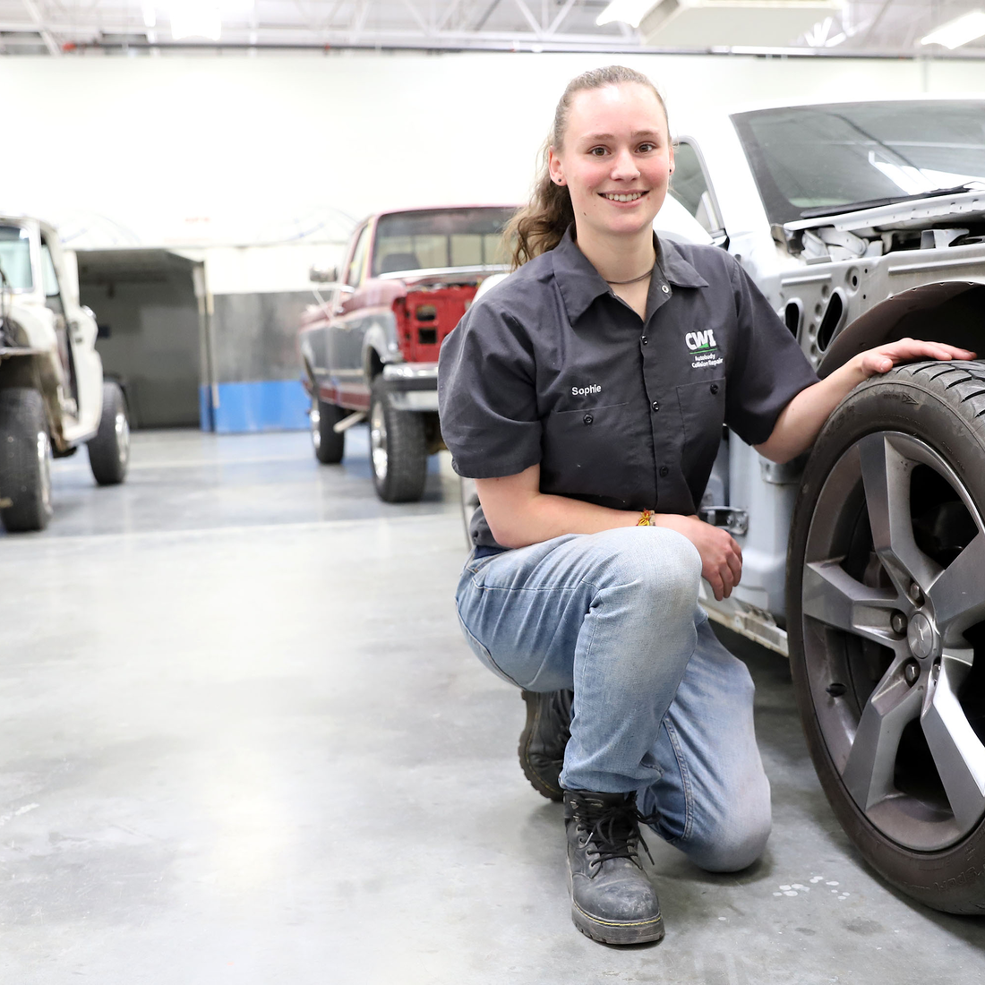 Sophie Rusling posing by a car in the Collision Repair Technology lab at CWI