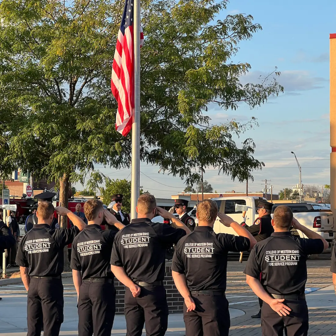 CWI Fire Service Program students saluting the American flag during a ceremony, with uniformed firefighters standing nearby.