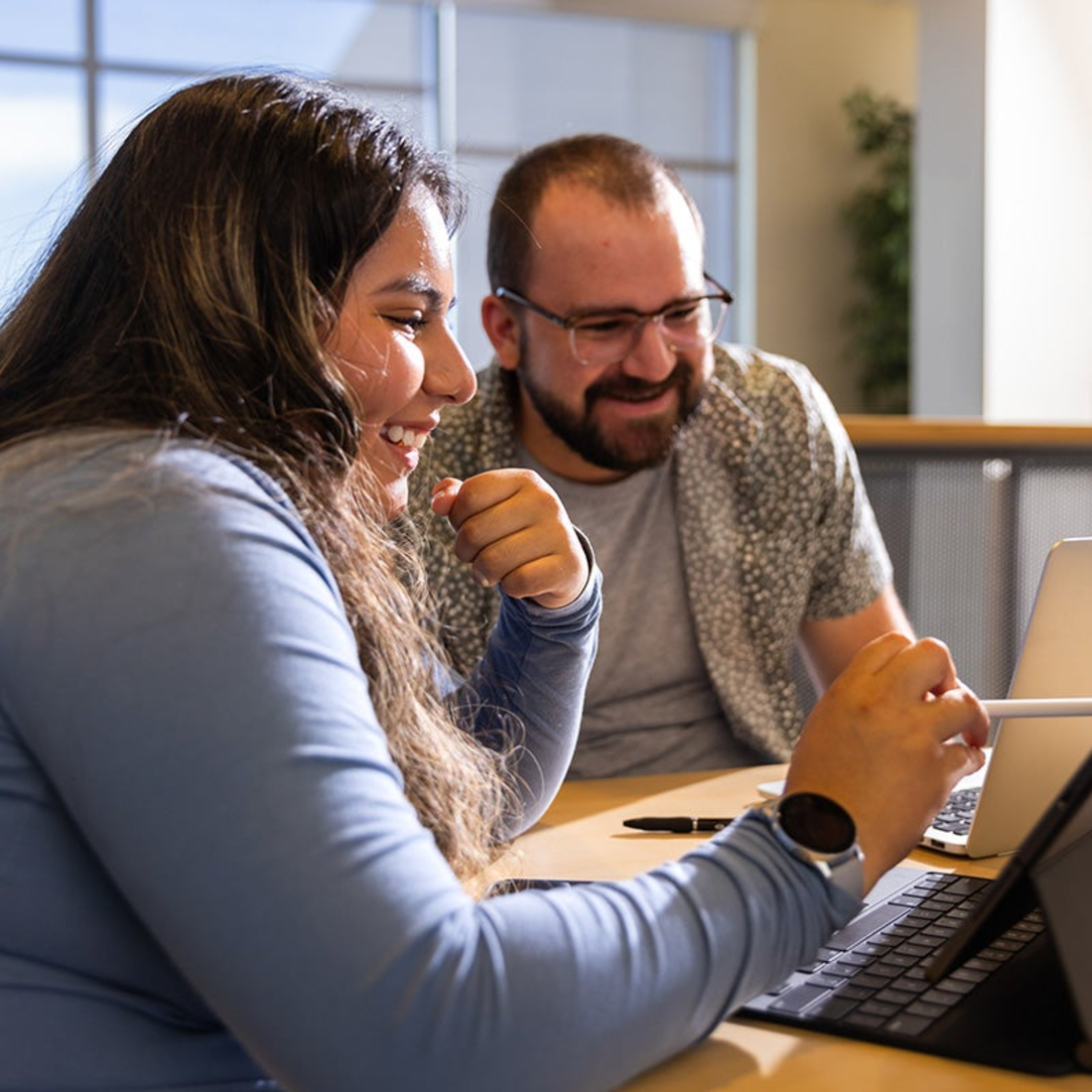 Two people conversing while studying on laptops