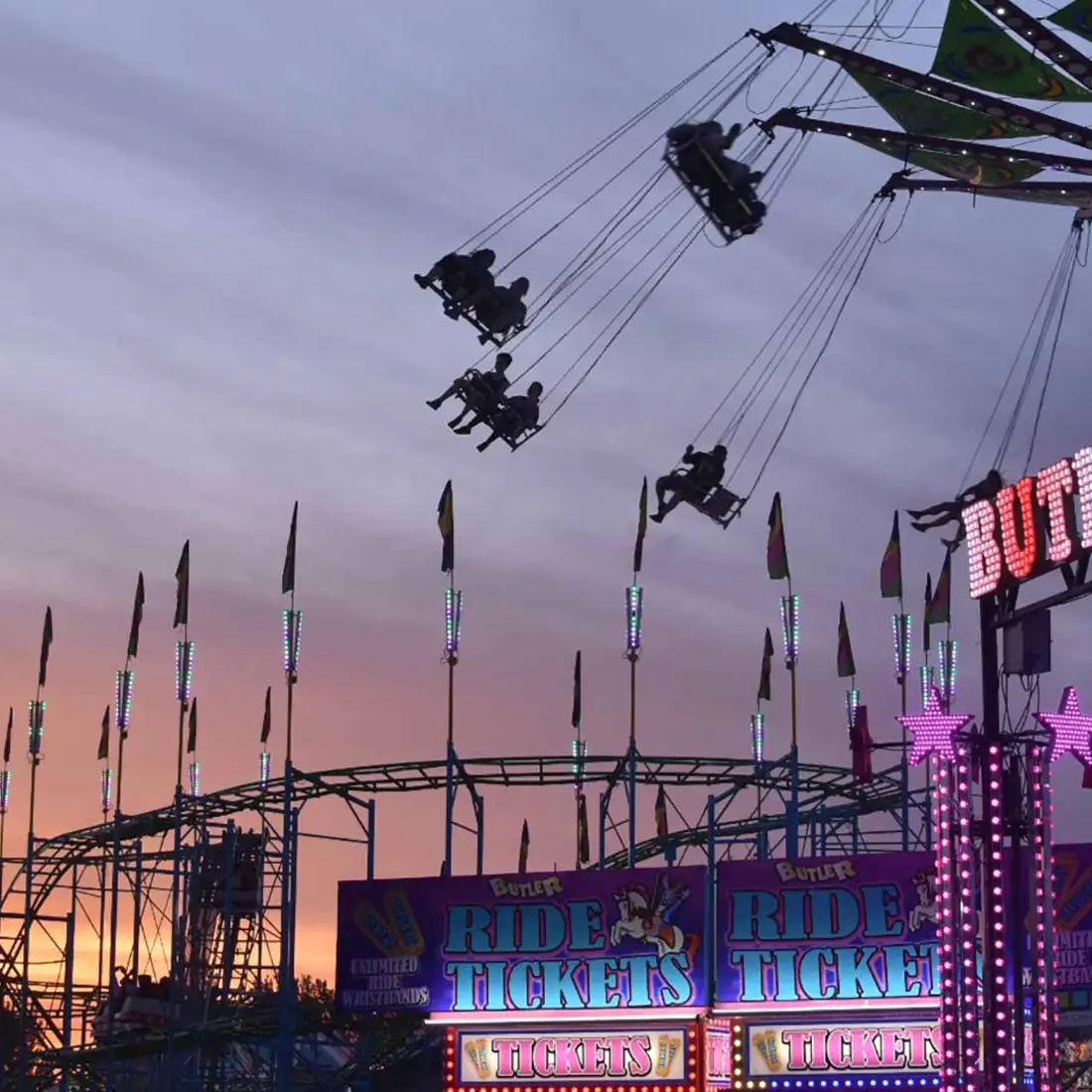 A photo of a fair showing a roller coaster and other rides being enjoyed by guests.