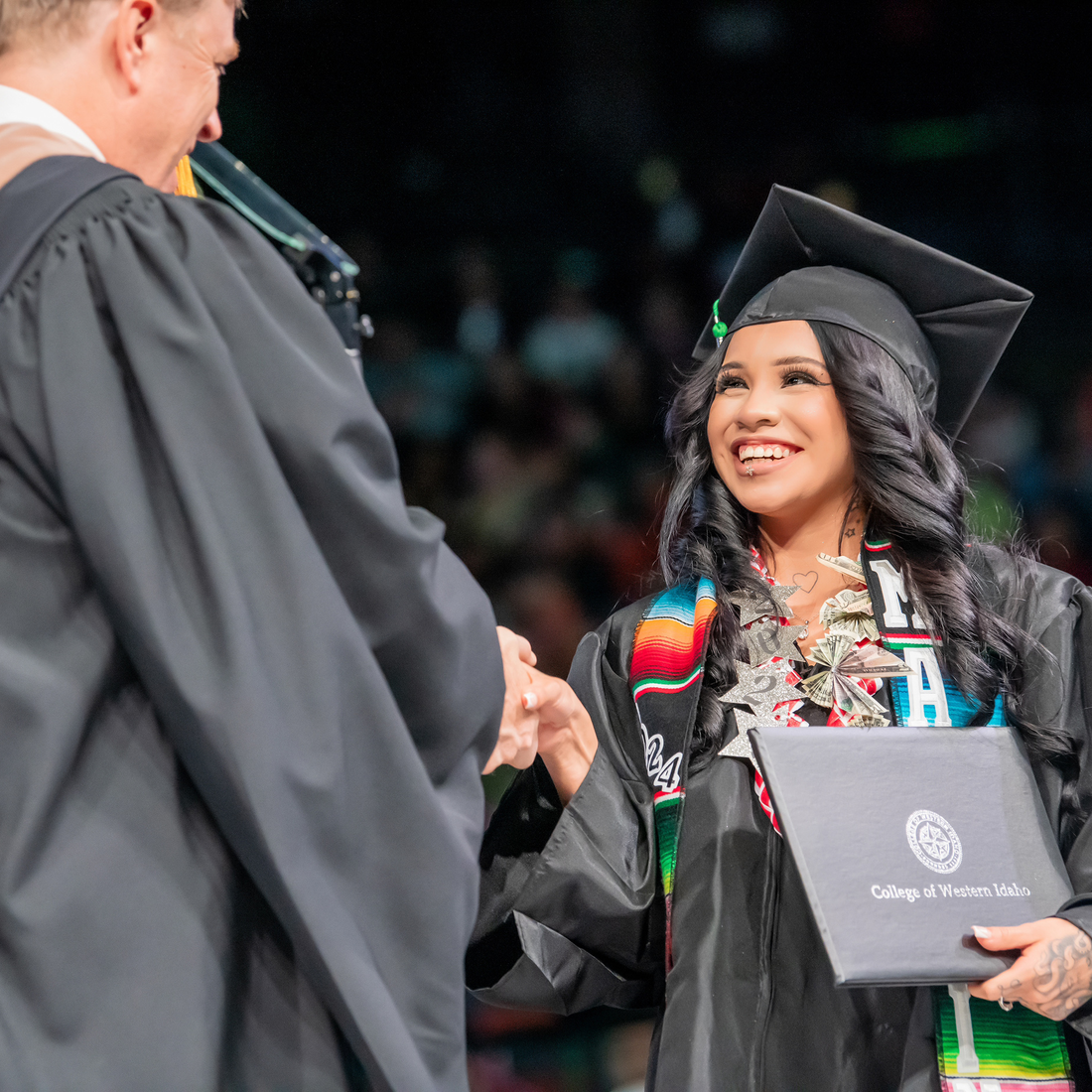 A student graduate in cap and gown accepts her degree with a handshake.