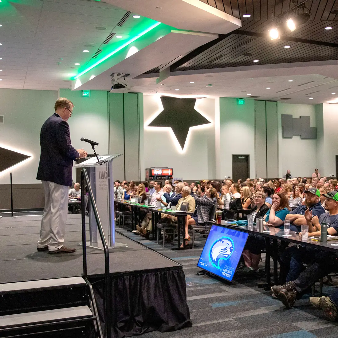 A speaker stands at a podium addressing a large audience.
