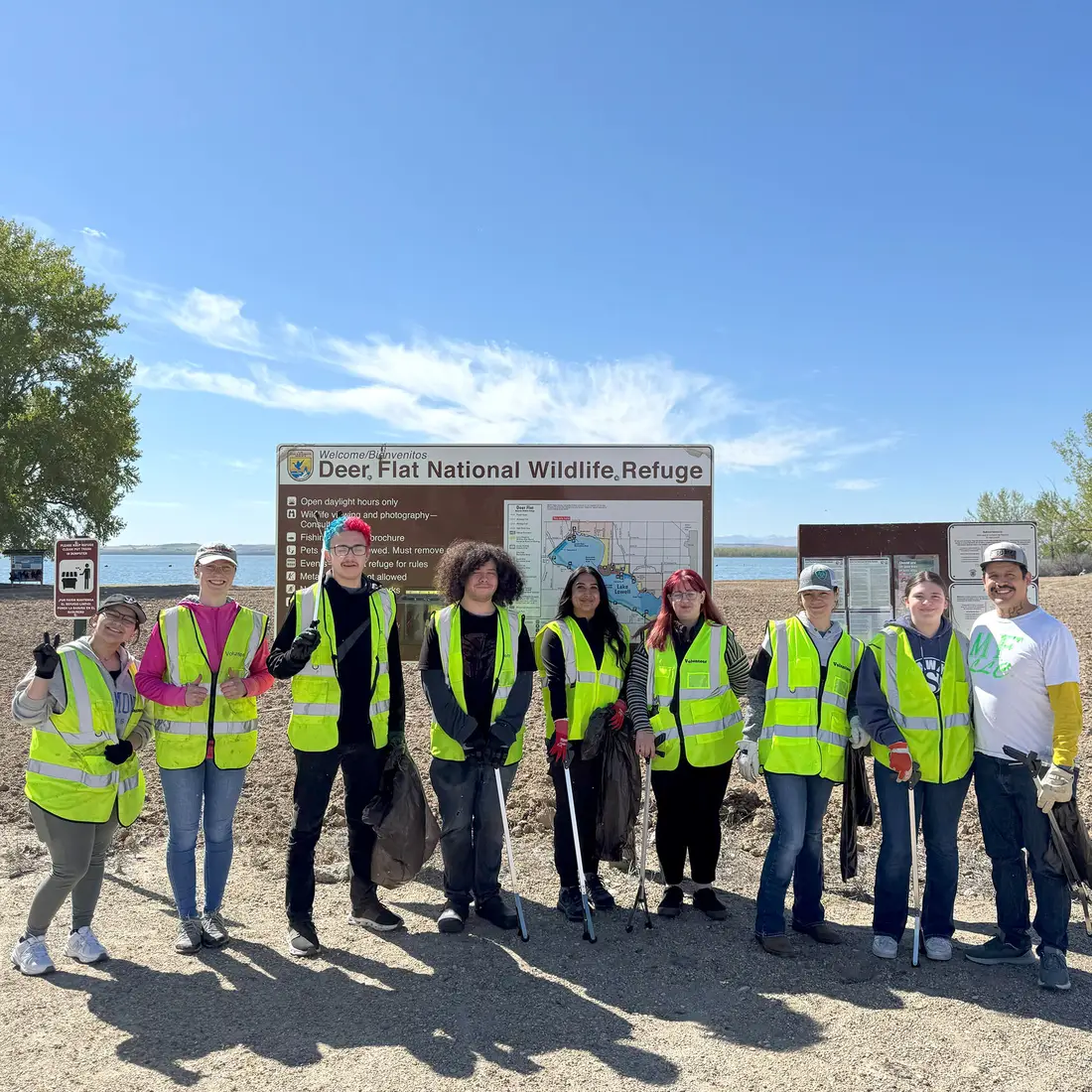A group of volunteers pose at a park holding trash bags and rakes.