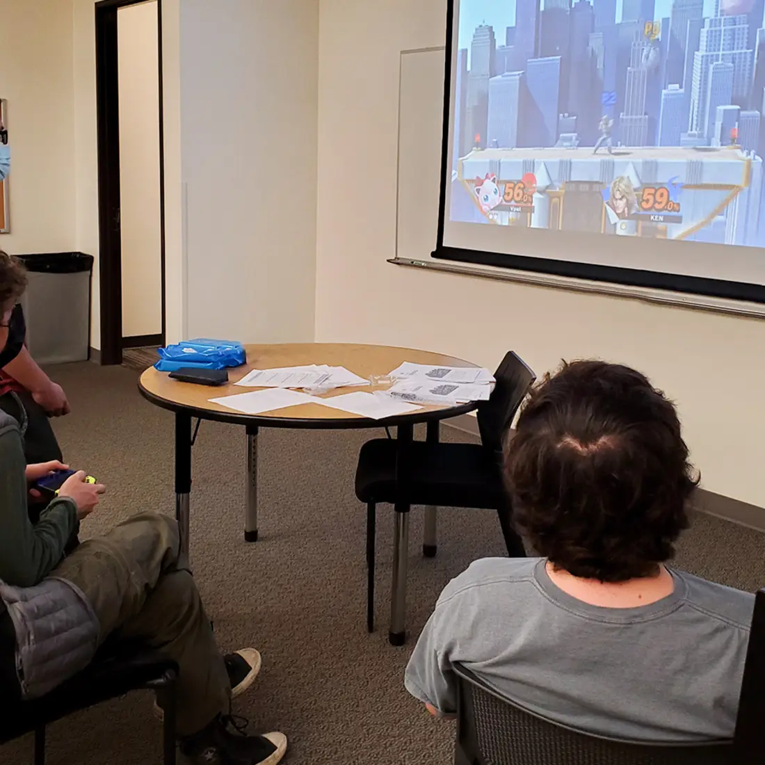 Three students playing a video game in a classroom on campus