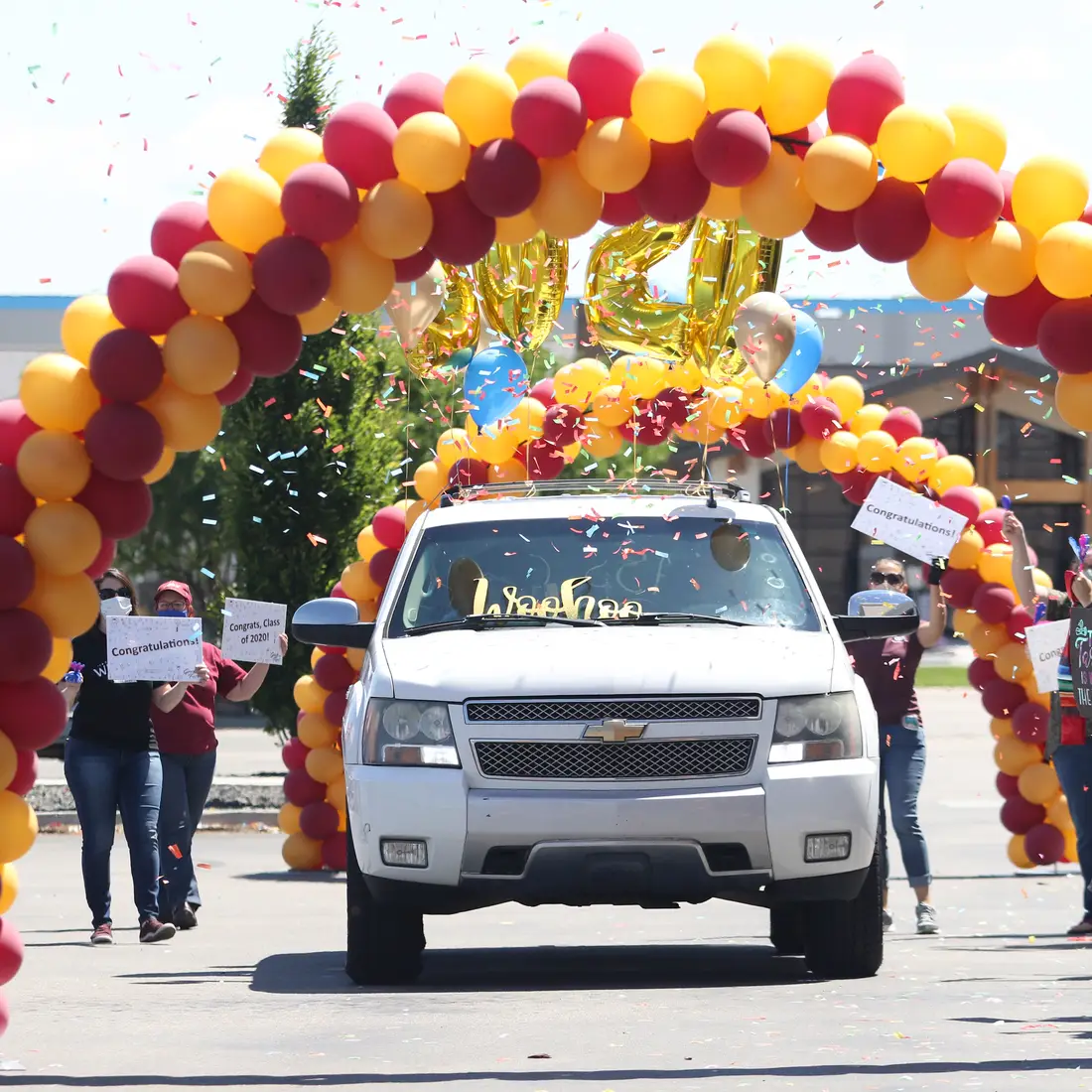 Car driving through an arch of balloons with confetti falling and people cheering