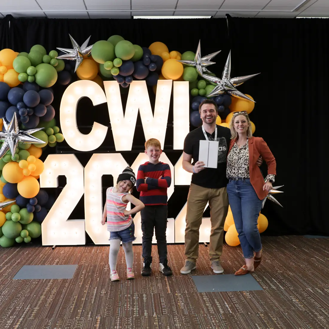 A graduate with his family in front of Alpha-Lit sign posing for a photo