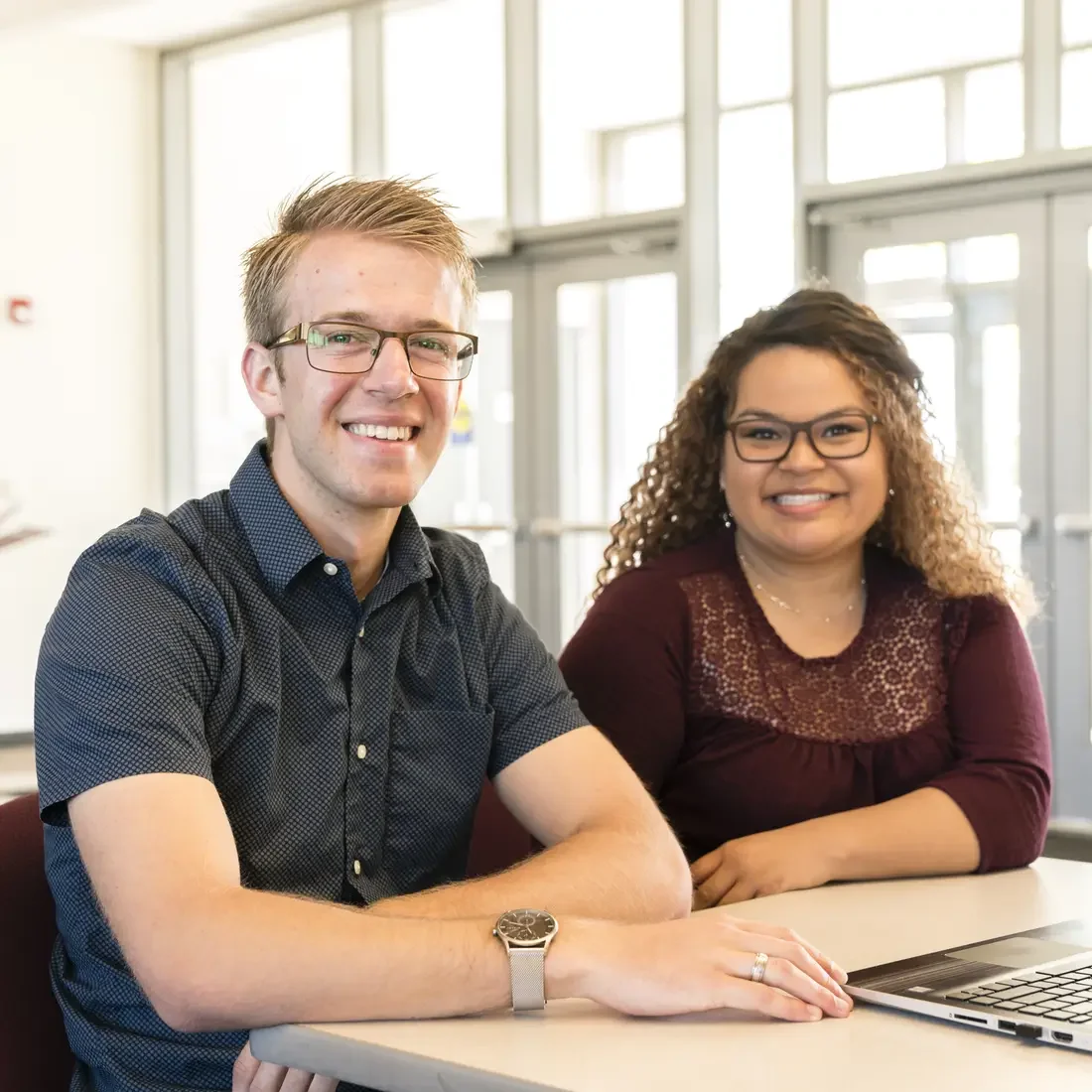 Two students sitting at a desk with a laptop on campus