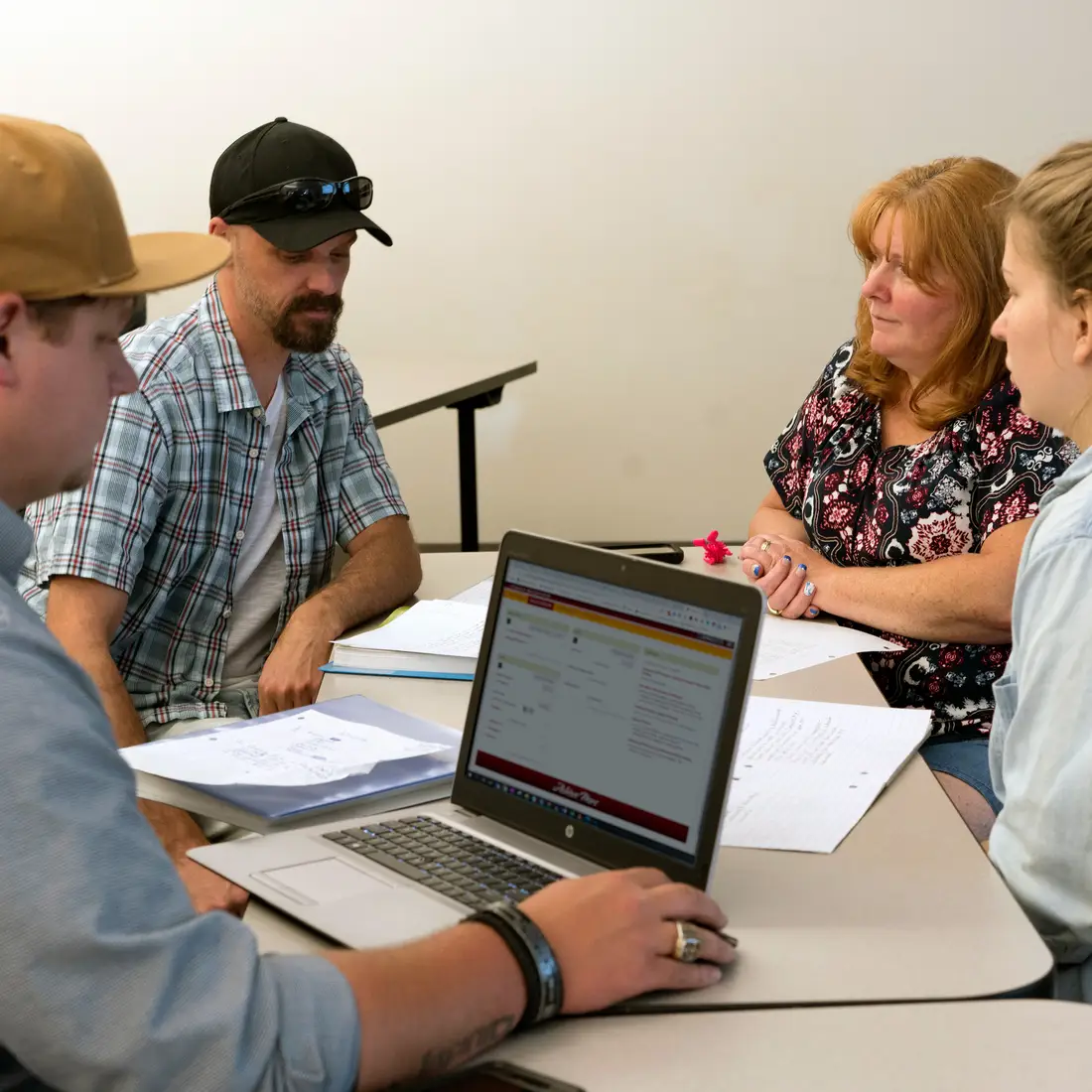 Four students sitting at a table together with a laptop having a conversation
