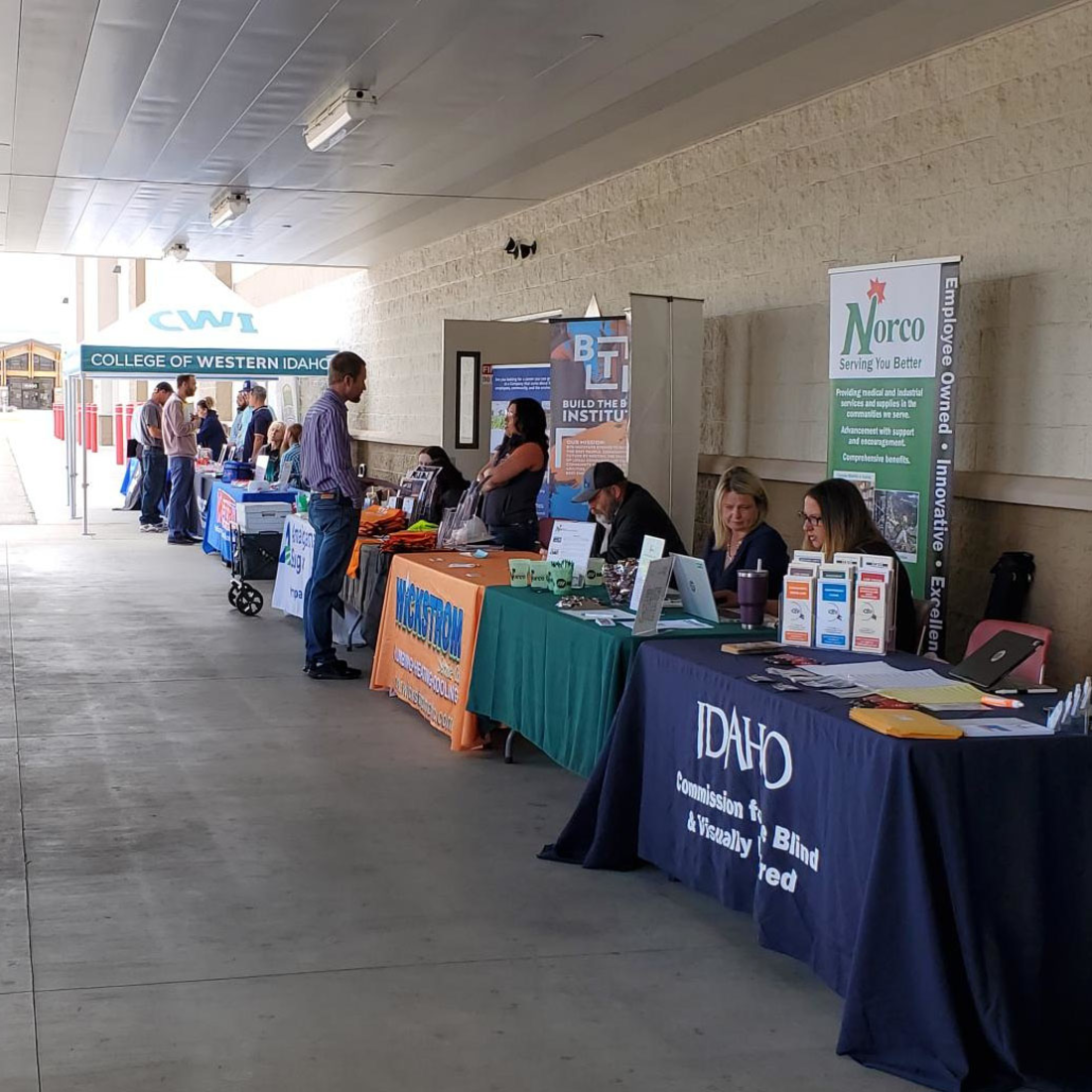 Students speak with potential employers who sit at a long line of tables that hold brochures and other materials.