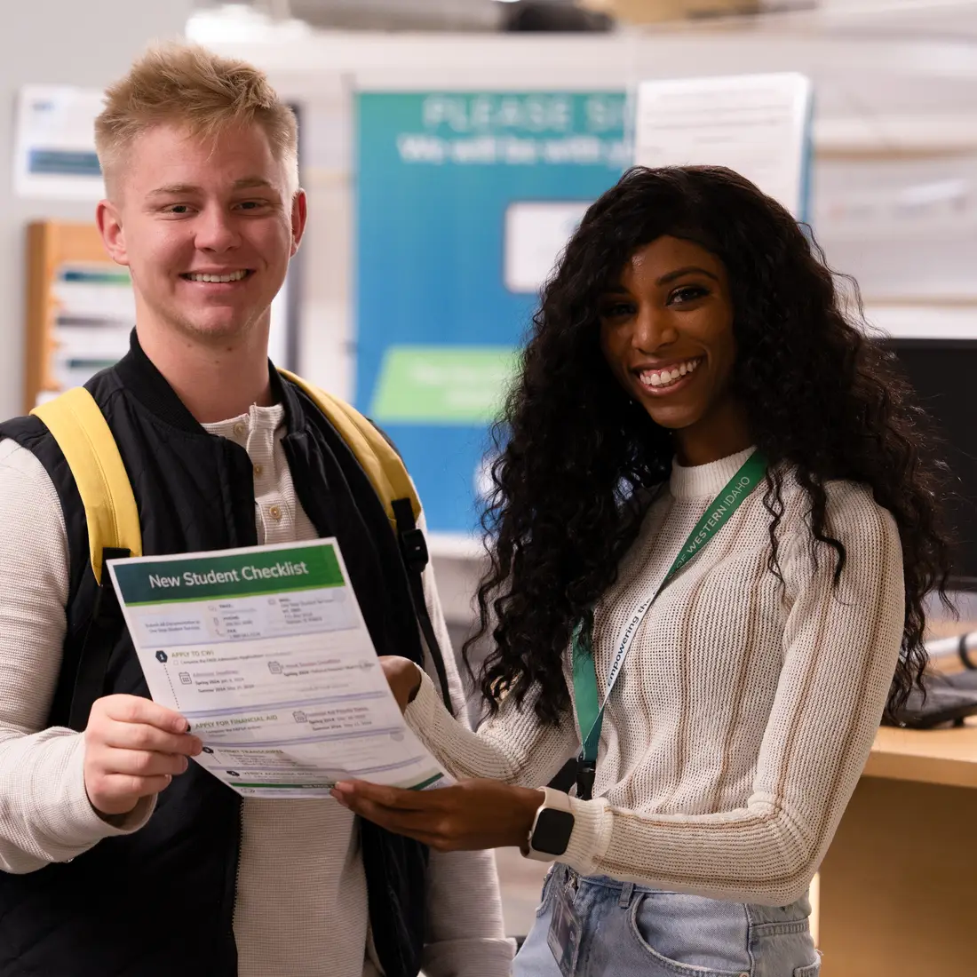 Two people standing together looking at a document and smiling at the camera