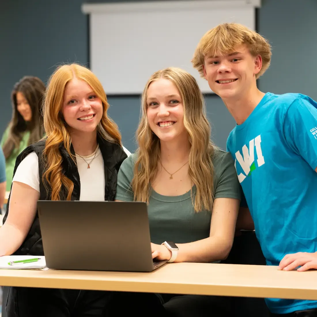 Three smiling students sit together in a classroom.