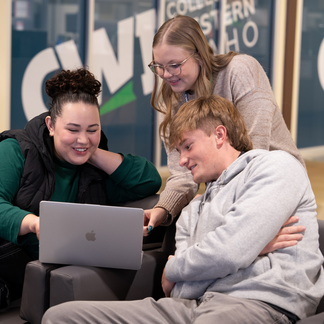 Three people sitting on a couch looking at a laptop
