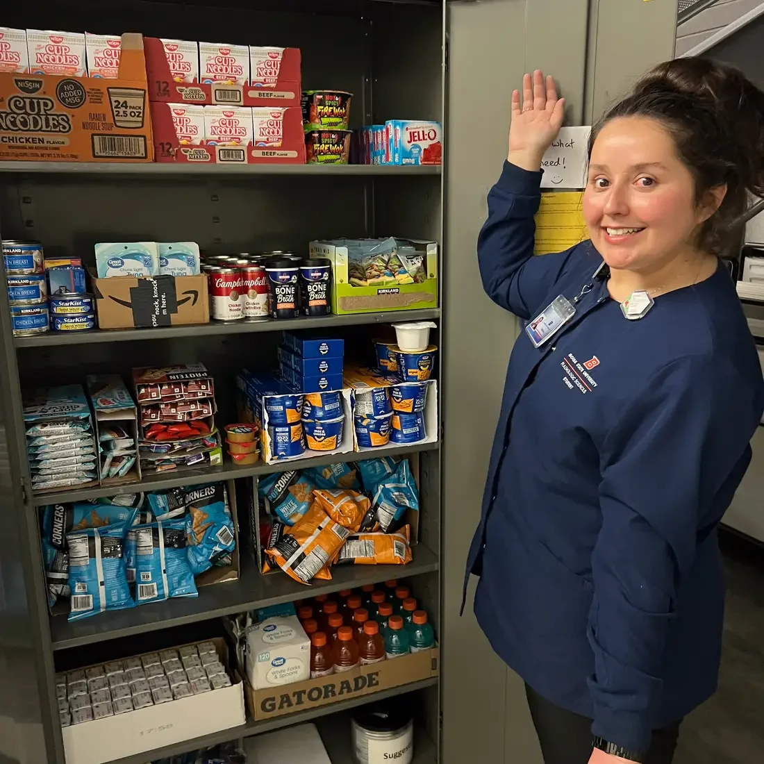Jeleana Loa posing in front of newly fully stocked Food Pantry