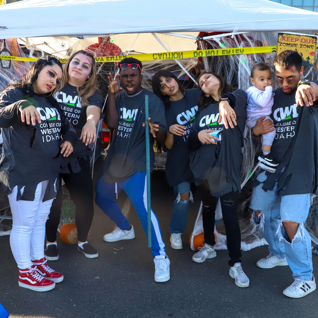Students dressed in Halloween costumes pose in front of a table with candy on it.