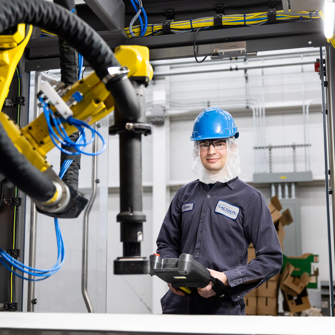 A mechatronics technician stands by a robotic machine in a manufacturing facility. 