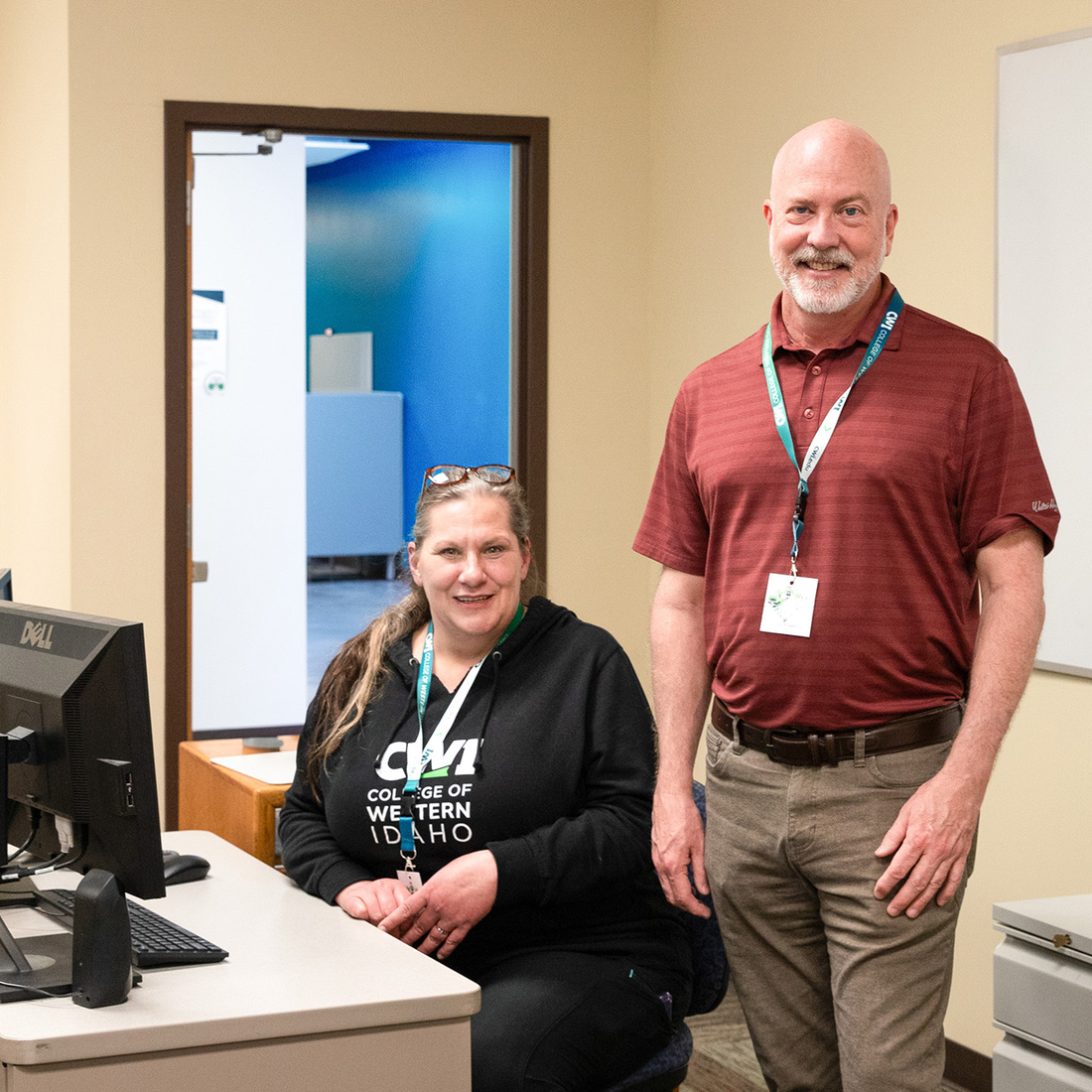 Two workers stand next to a desk posing for a photo. 