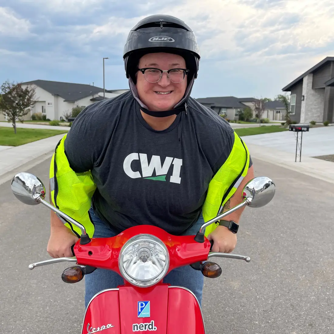 Faculty member, Maia Kelley, riding a moped and wearing a newly-branded CWI shirt