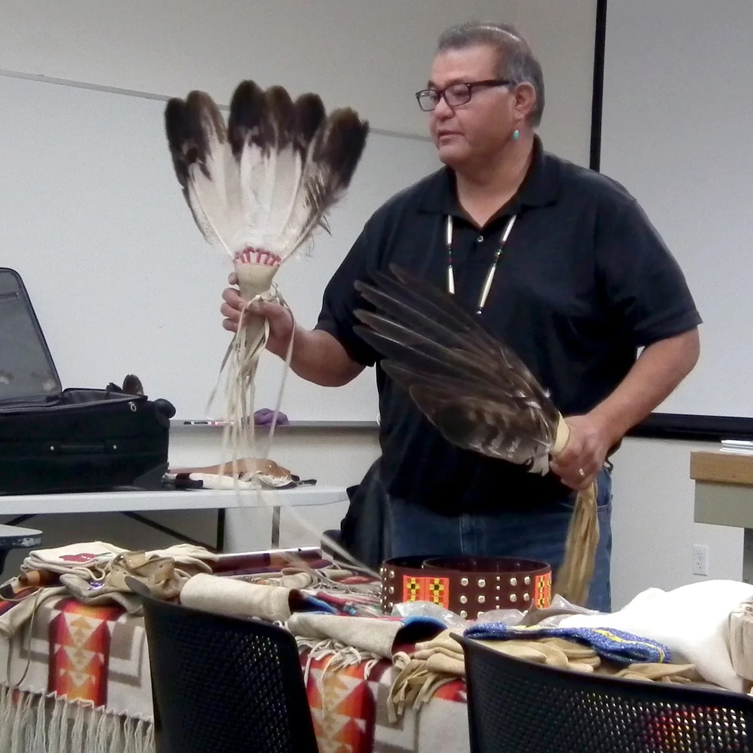 A Native American man demonstrates traditional ceremonial pieces in front of a class.