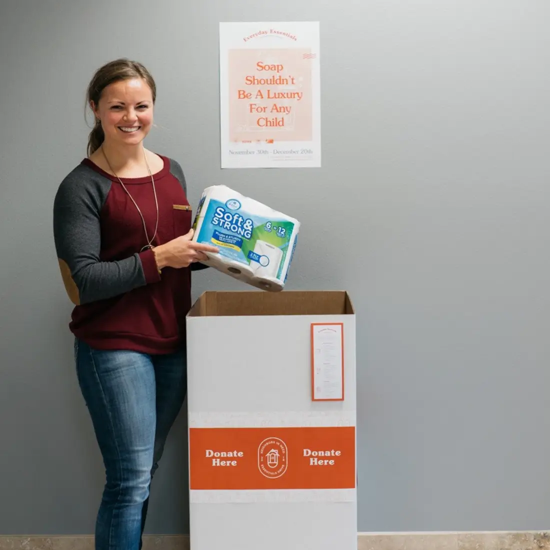 Woman standing by donation box holding donation of toilet paper