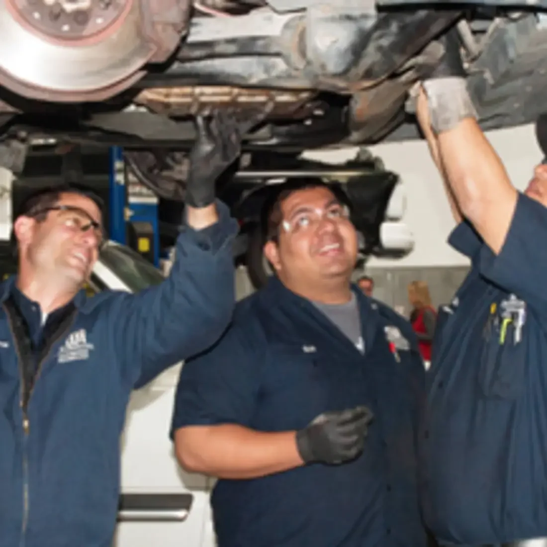 Three students working under a vehicle in the auto class.
