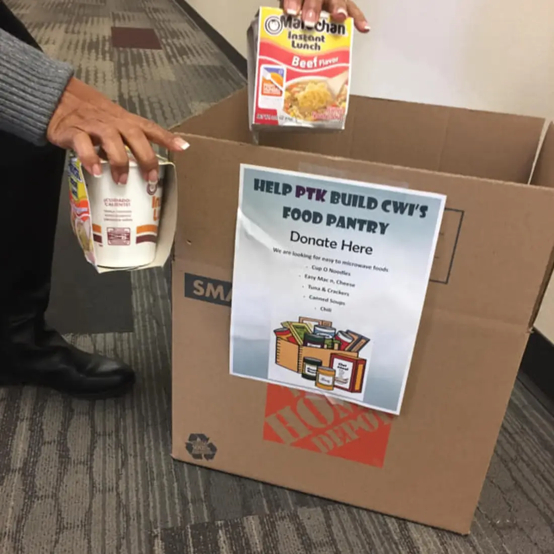 Individual placing canned food items in donation box. 
