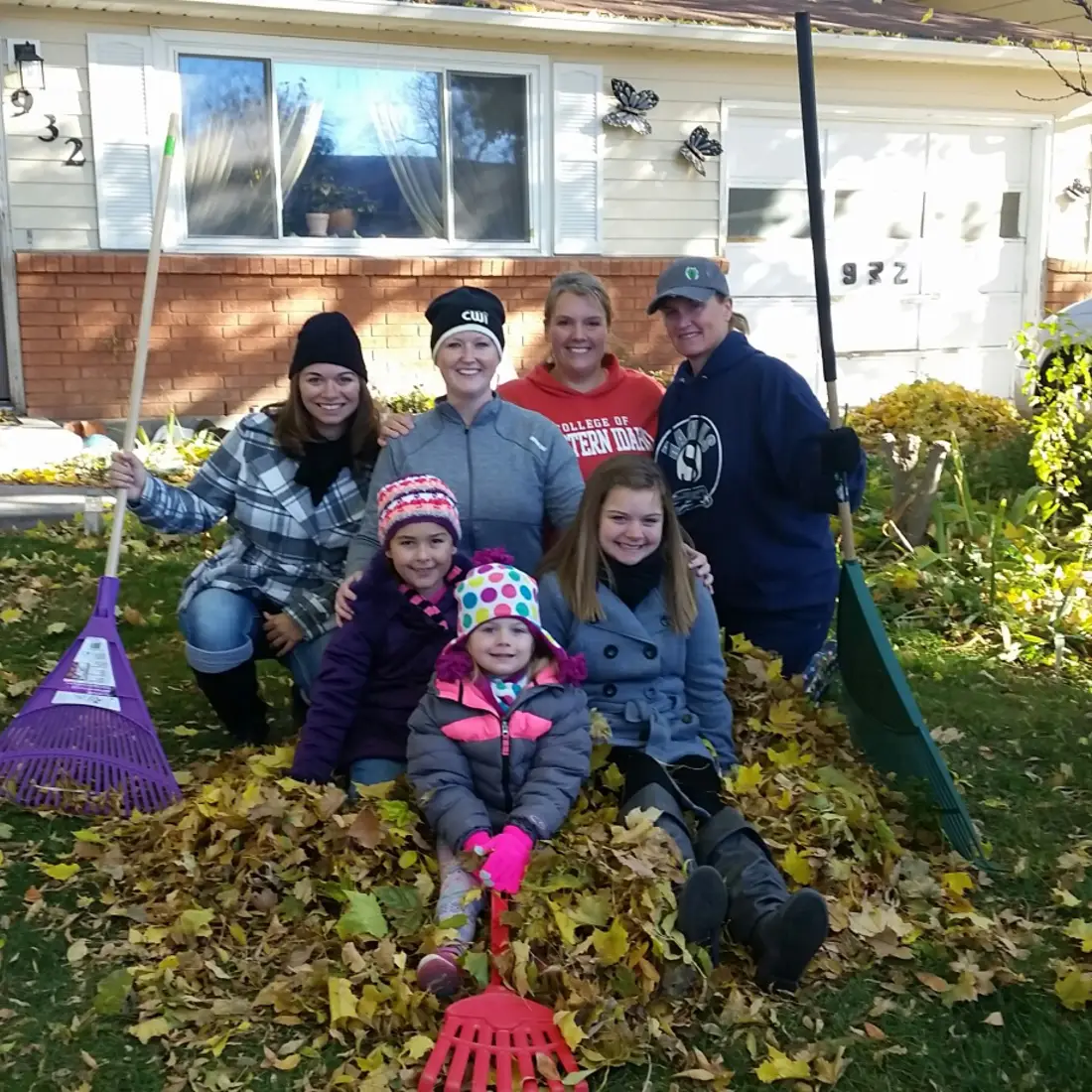 Employees raking up community event posing with leaves and rakes