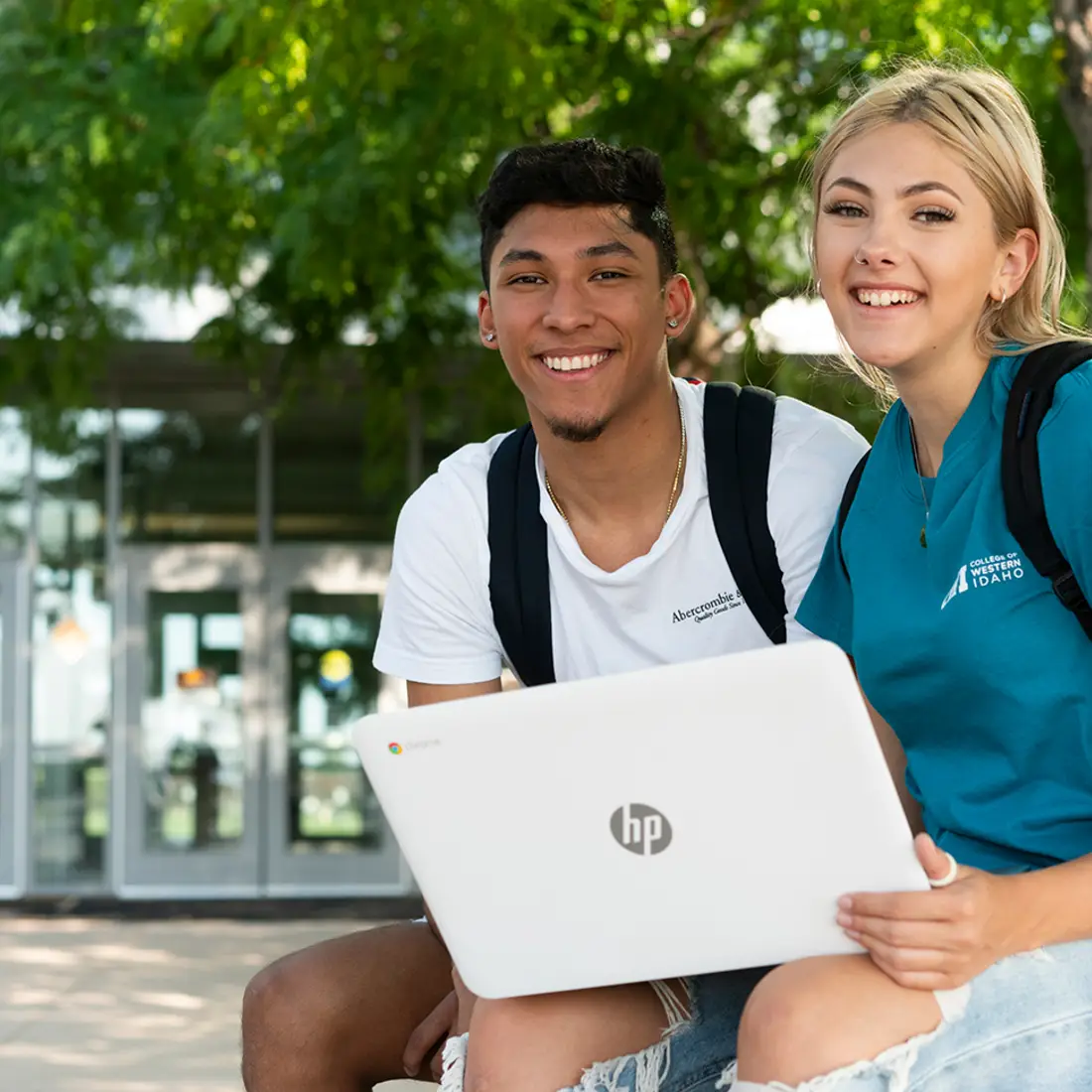 Students sitting outside Nampa Campus Academic Building with a laptop