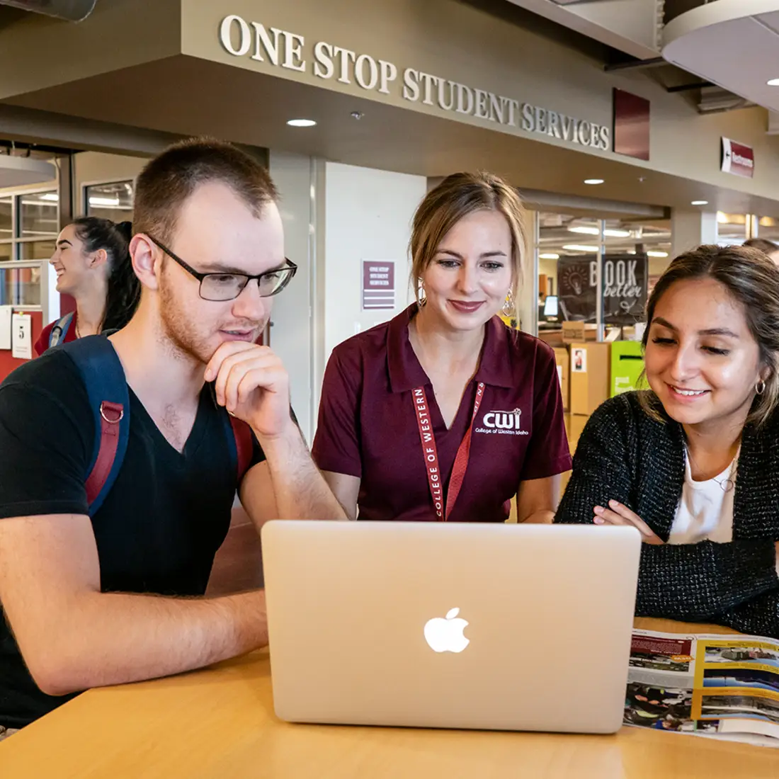 Students and an advisor at a laptop surrounded by other students near One Stop Student Services