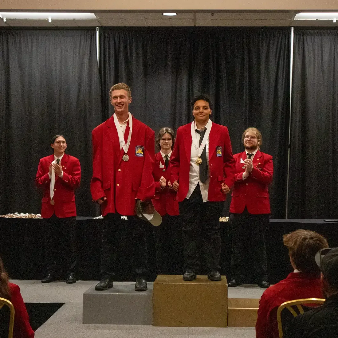 Five individuals in red blazers stand on a stage during an award ceremony.