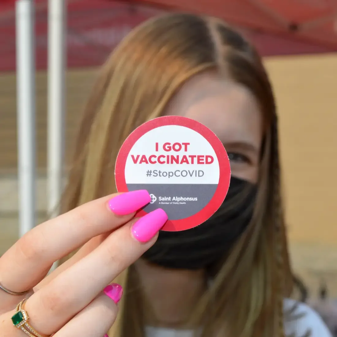 Woman holding up a sticker stating vaccination status