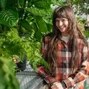 Student stands in greenhouse in front of several plants