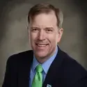 Studio headshot of a smiling man wearing a navy suit, light blue shirt, and green tie against a neutral background