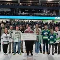 Group of college representatives present a scholarship check on the ice at a hockey arena.