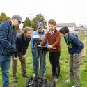 Five people stand on grass while looking at a screen 