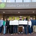Group of people with bear mascot holding two checks