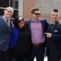 group of alumni with arms around each other, dressed up, outside, smiling at the camera