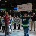 Student stands on hocky rink holding up large check with people surrounding them
