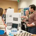 Person stands next to presentation board chatting with another person
